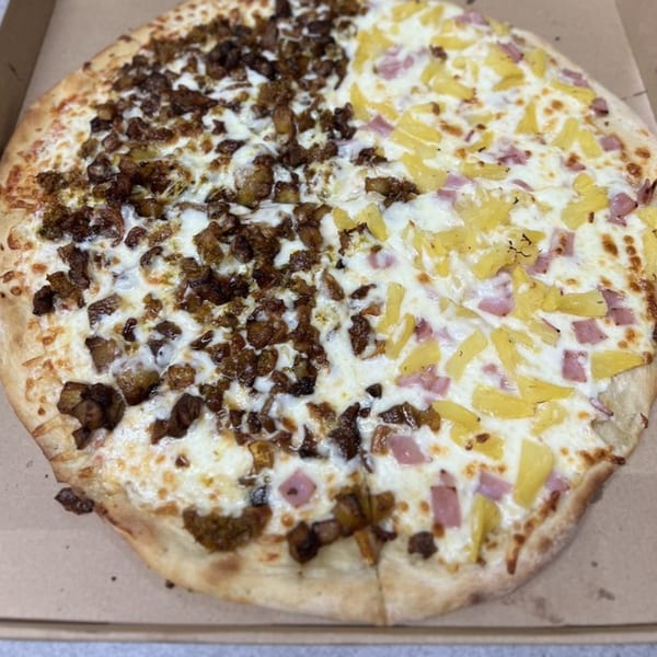 A half-and-half pizza with one side topped with meat and the other with pineapple and ham.