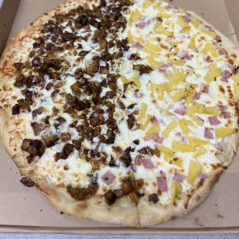 A half-and-half pizza with one side topped with meat and the other with pineapple and ham.