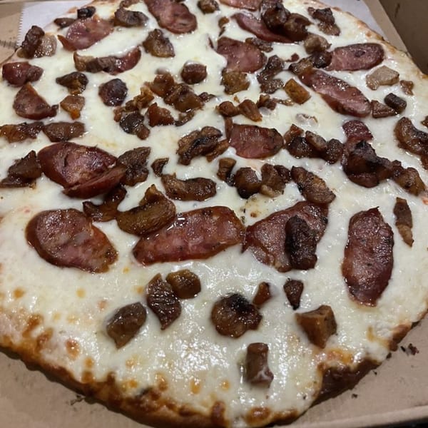 A close-up of a Tato's Pizzeria pizza with melted cheese, sausage, and bacon toppings.